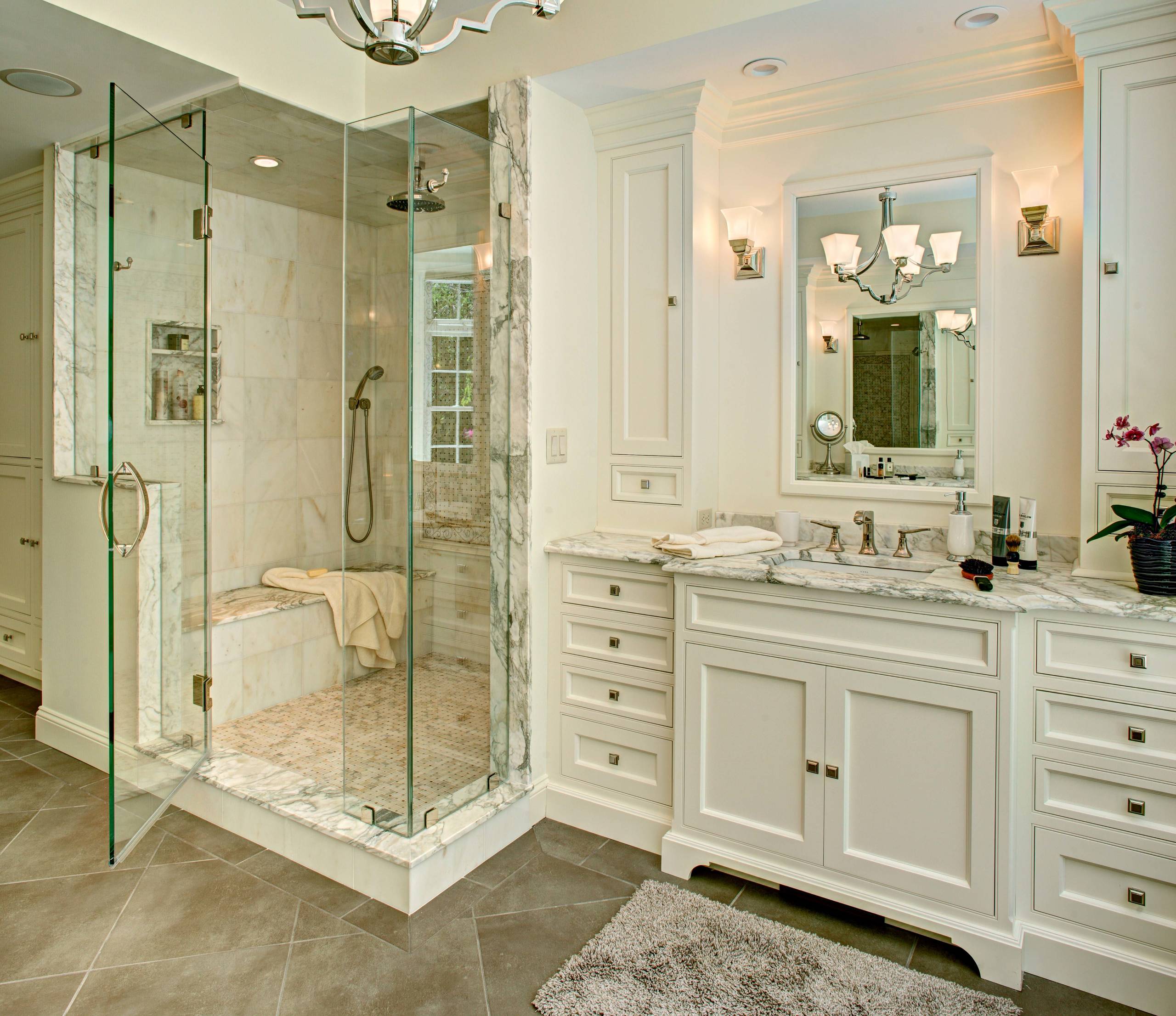 Luxury bathroom with glass shower, marble surfaces, and classic white vanity.