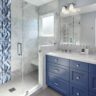 Bathroom with blue vanity, marble countertops, and glass shower featuring decorative blue tile accent.