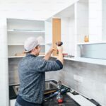 Kitchen remodeling expert installing upper cabinet shelves with a power drill