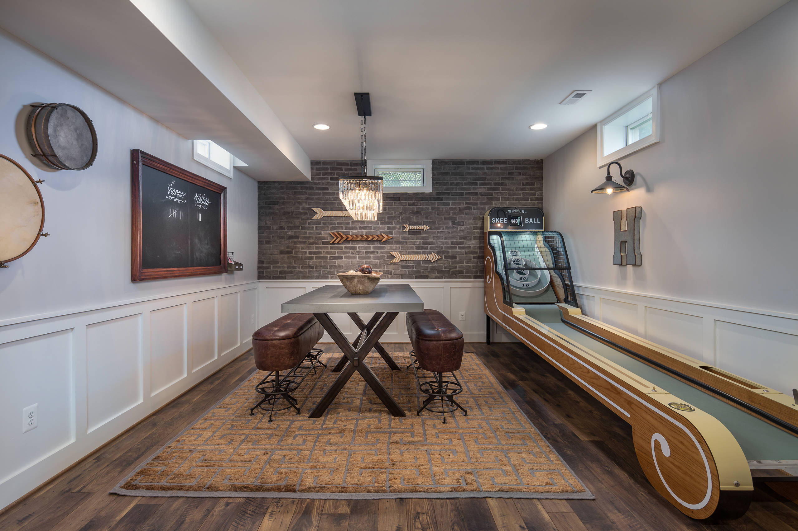 Rustic basement with game area, dining table, and skee-ball machine.