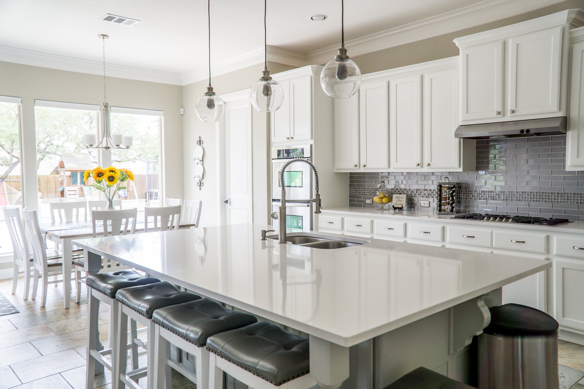 Bright white kitchen with a large island, gray backsplash, and dining area with sunflowers.