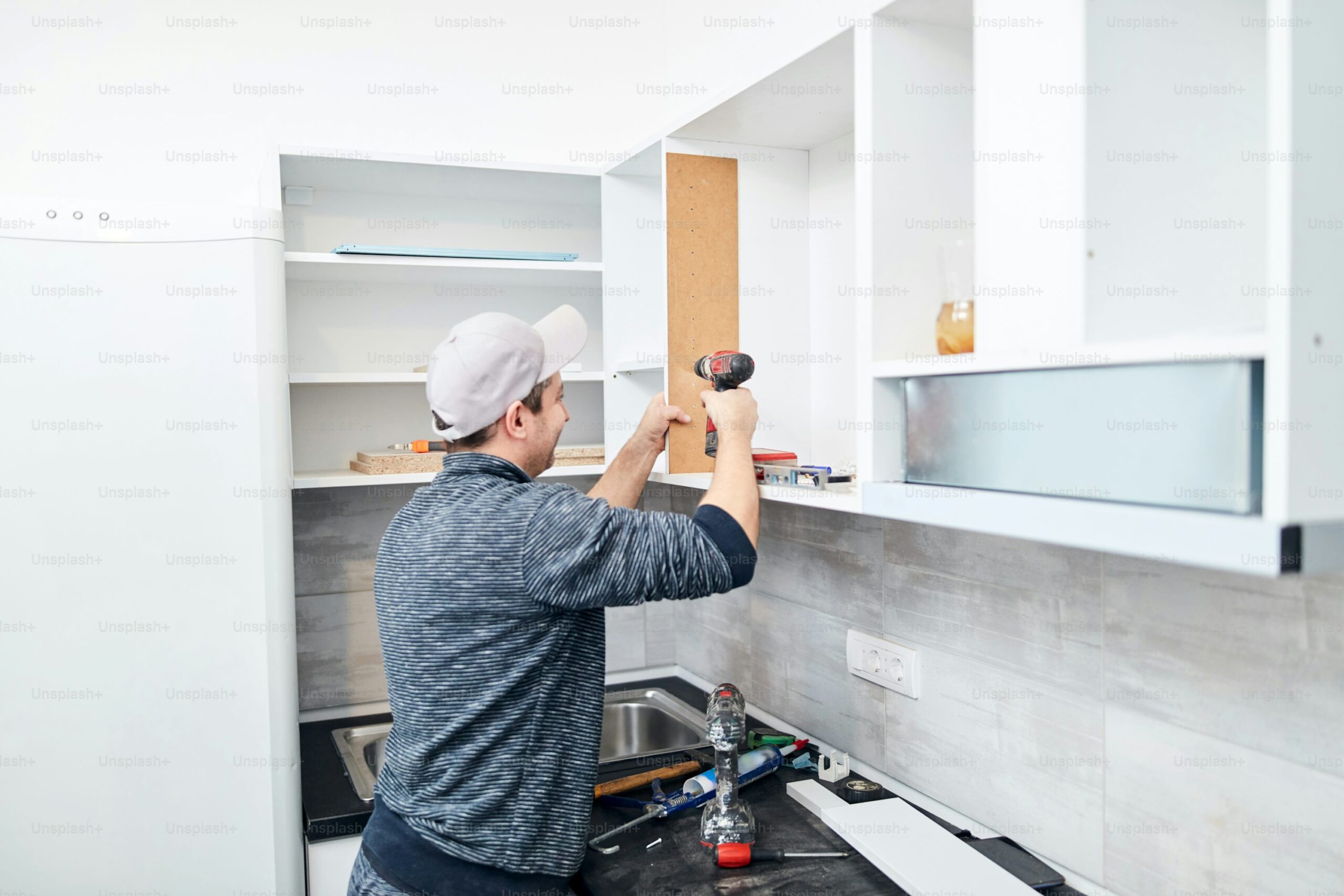 A man installing a kitchen cabinet using a power drill.
