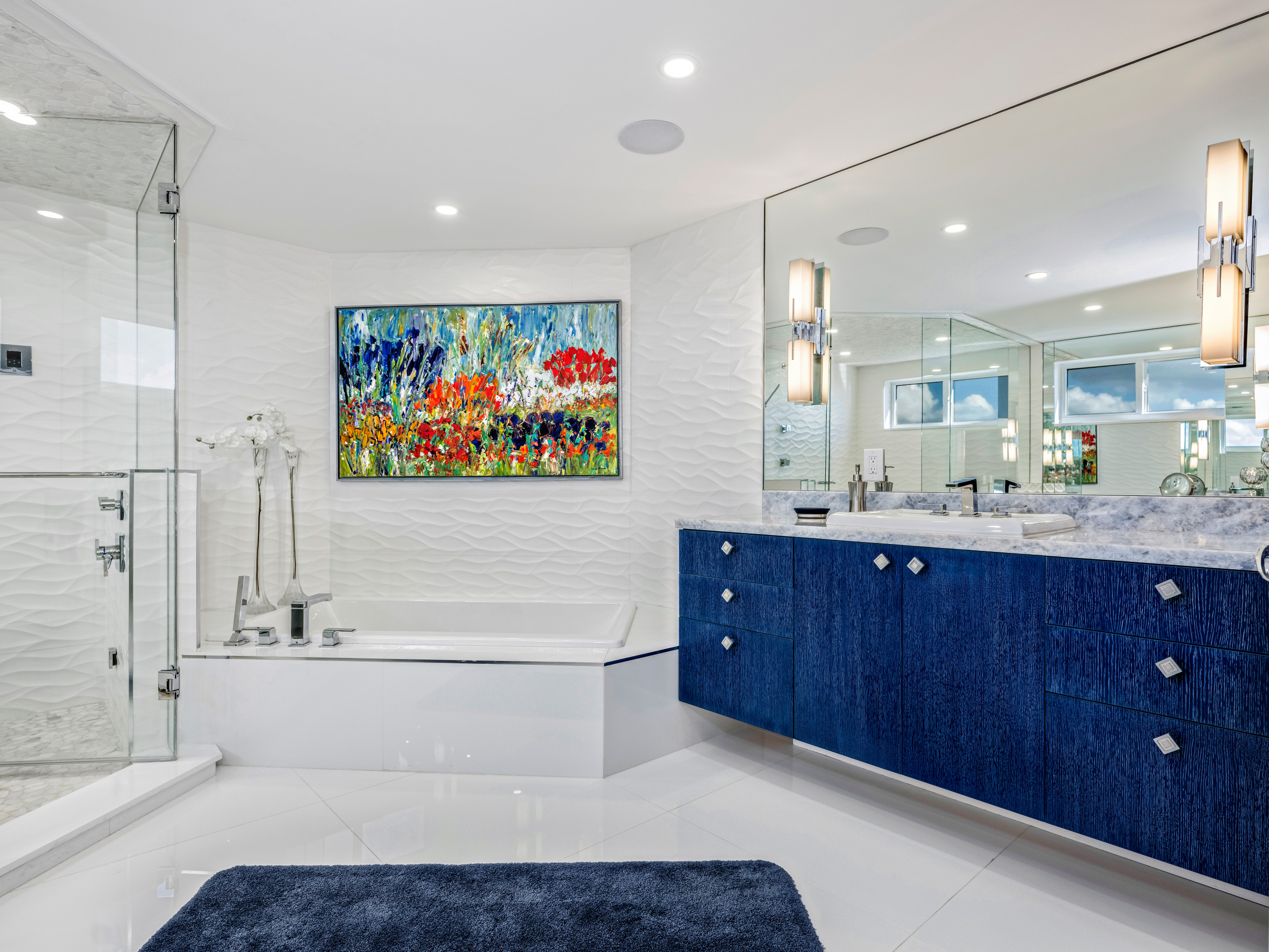 Modern bathroom with blue vanity, glass shower, and colorful wall art.