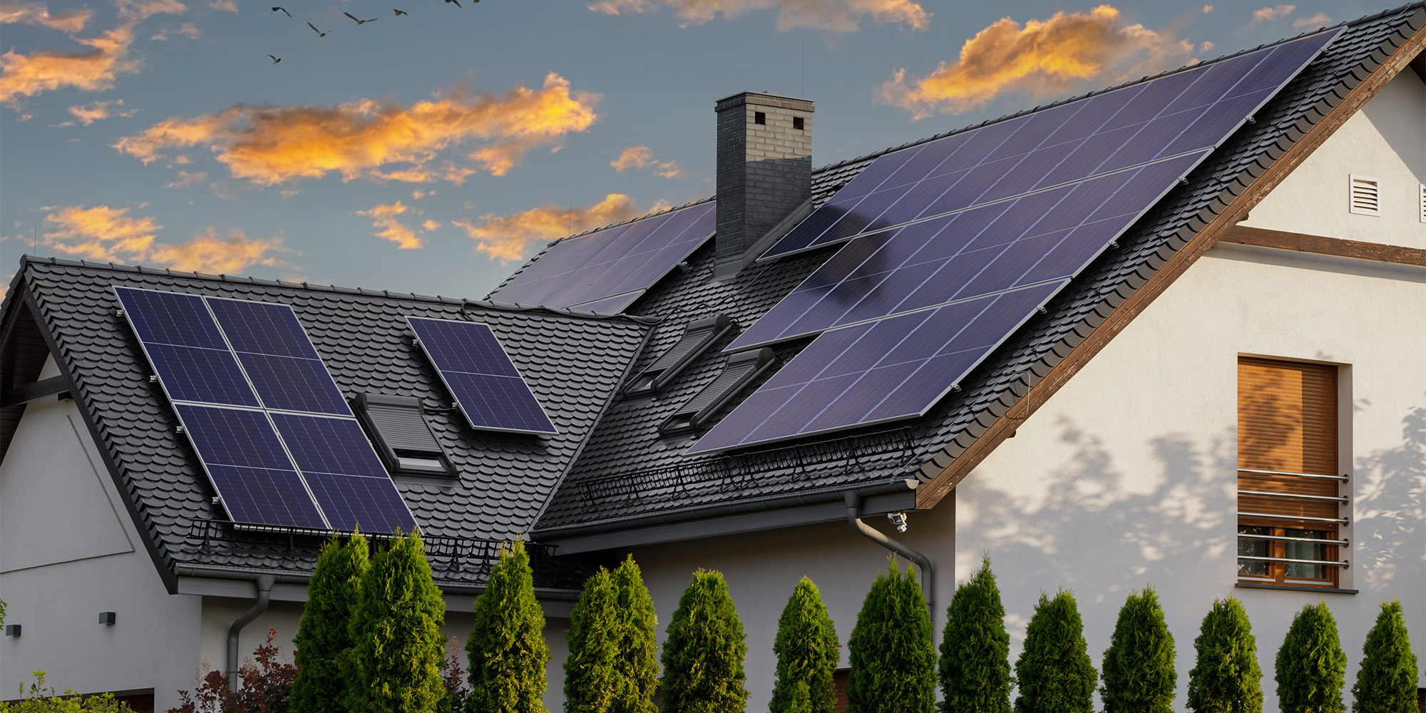 Modern house with rooftop solar panels installed on dark tile roof at sunset