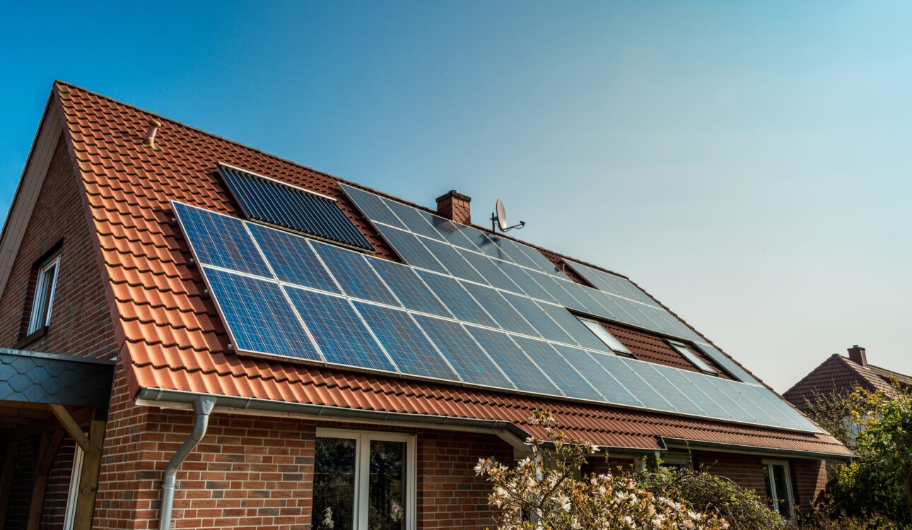 Brick house with red tile roof equipped with solar panels under a clear blue sky