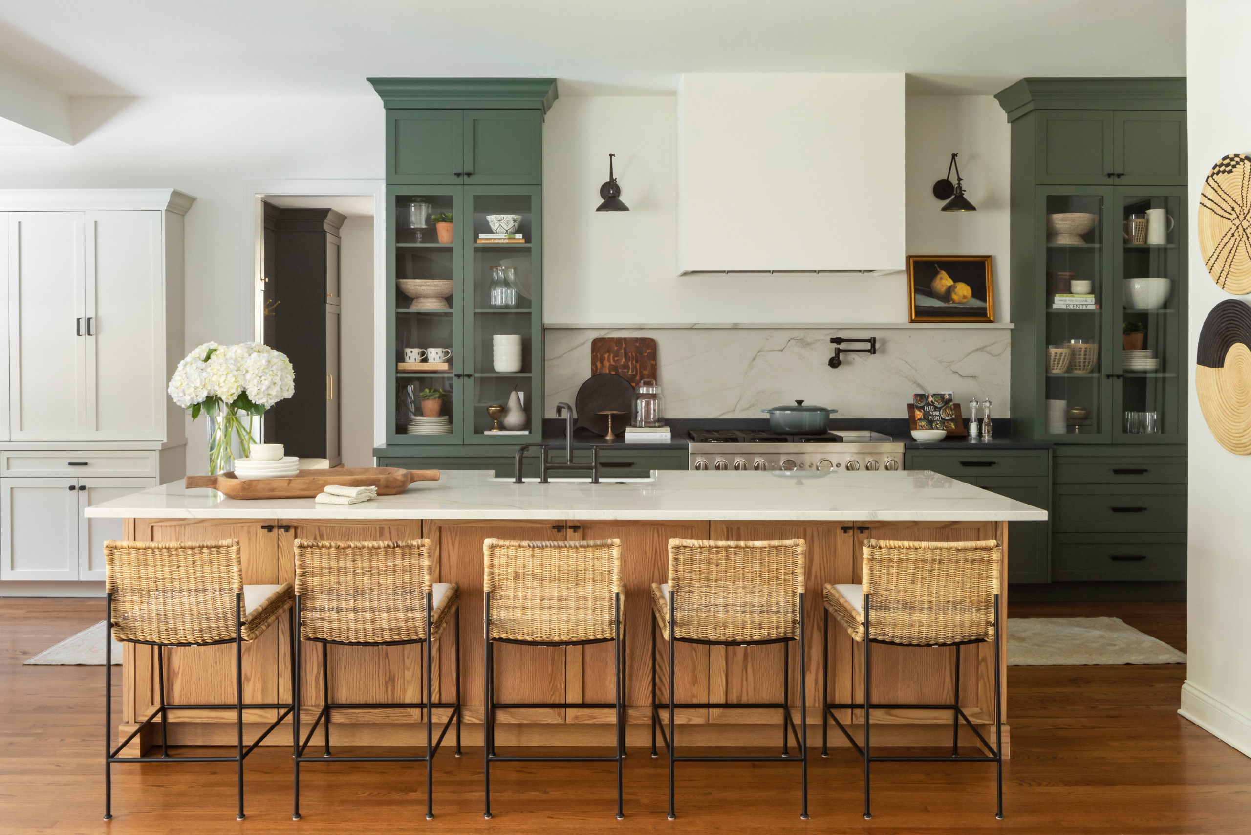 Stylish kitchen with green cabinets, marble backsplash, wooden island, and woven barstools.