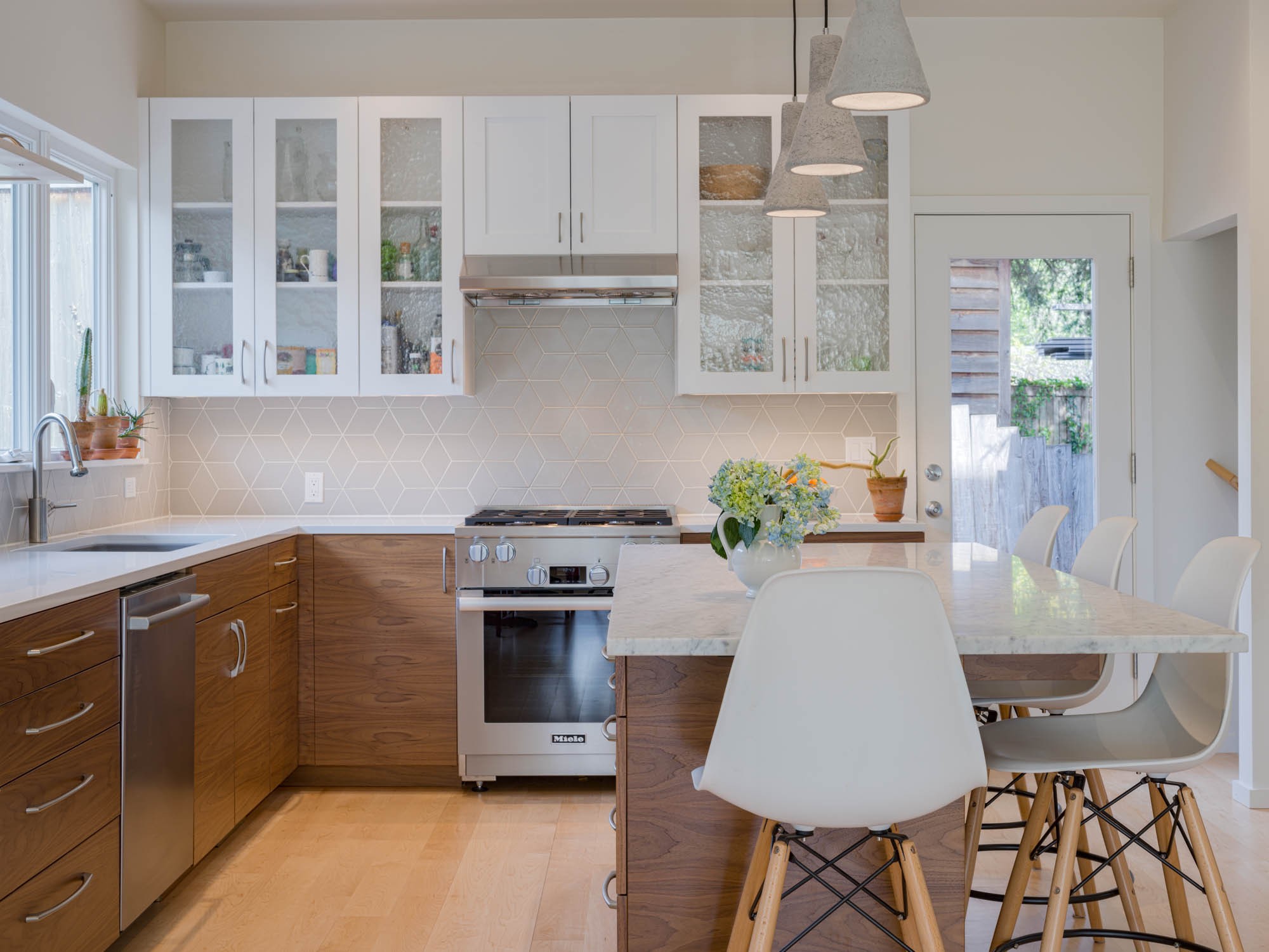 Modern kitchen with two-tone cabinets, glass upper doors, geometric backsplash, and marble island