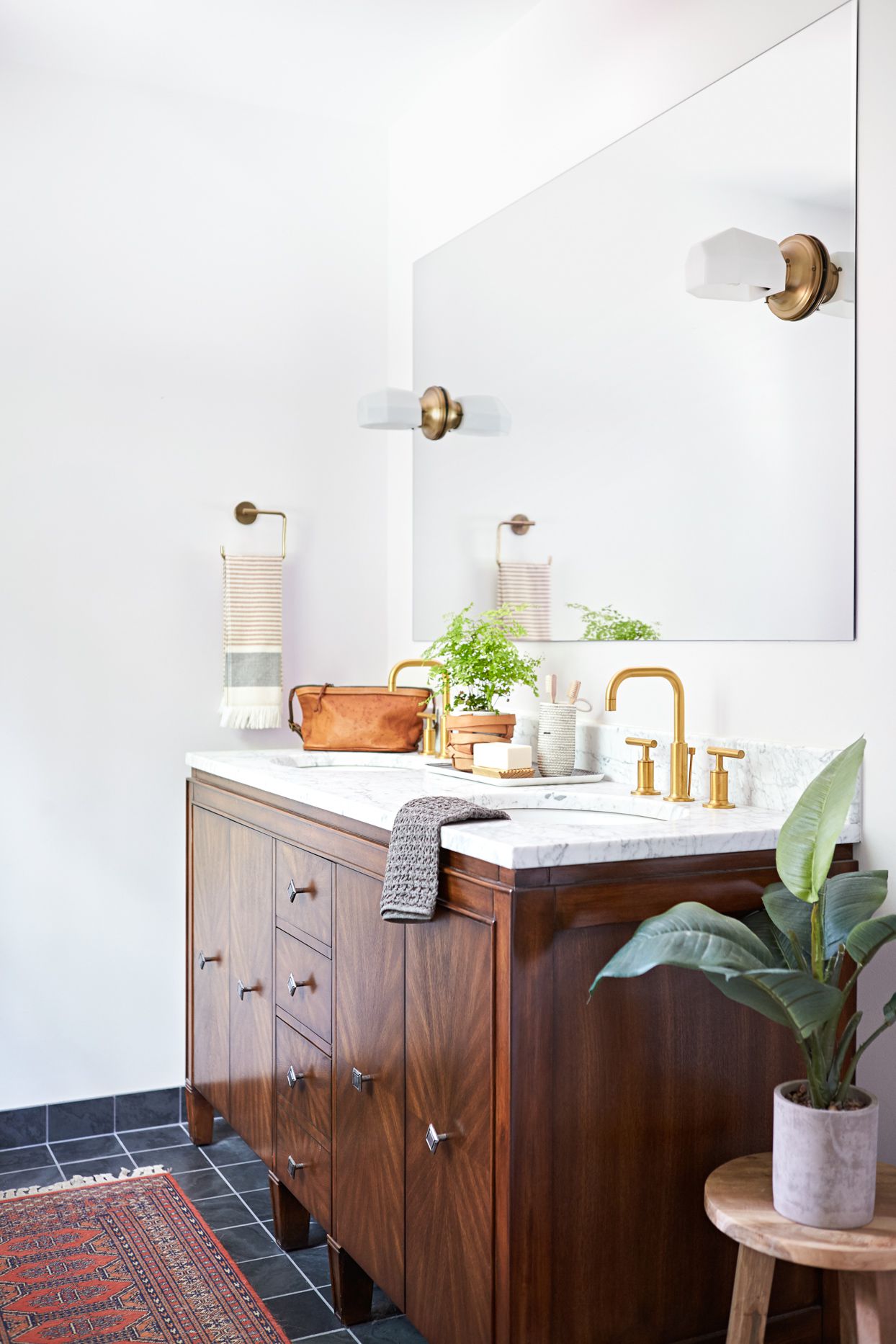 Stylish bathroom with wood vanity, marble countertop, gold faucet, and decorative plants